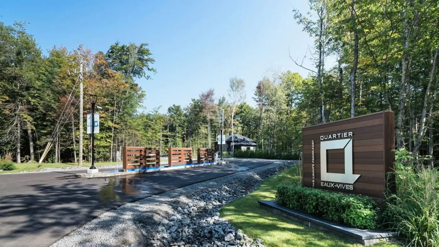 L'entrée du Quartier Eaux-Vives : la rue asphaltée, l'enseigne de bois avec le logo du quartier, la forêt d'érables derrière