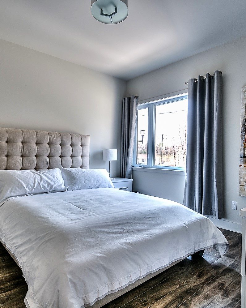 Chambre principale au Quartier Eaux-Vives : tête de lit capitonnée, plancher de bois, fenêtre sur la forêt